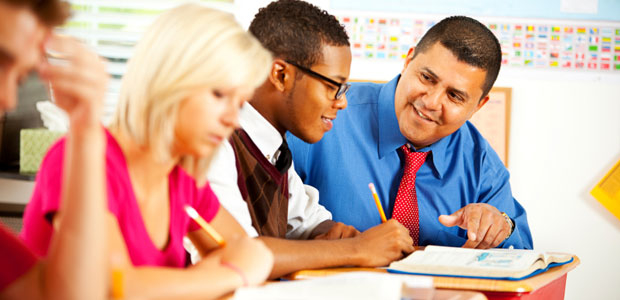 Contact us to find out more about ZAPS seminars and Score Boosters. A smiling Hispanic male teacher works with a smiling African American teenager in a diverse class.